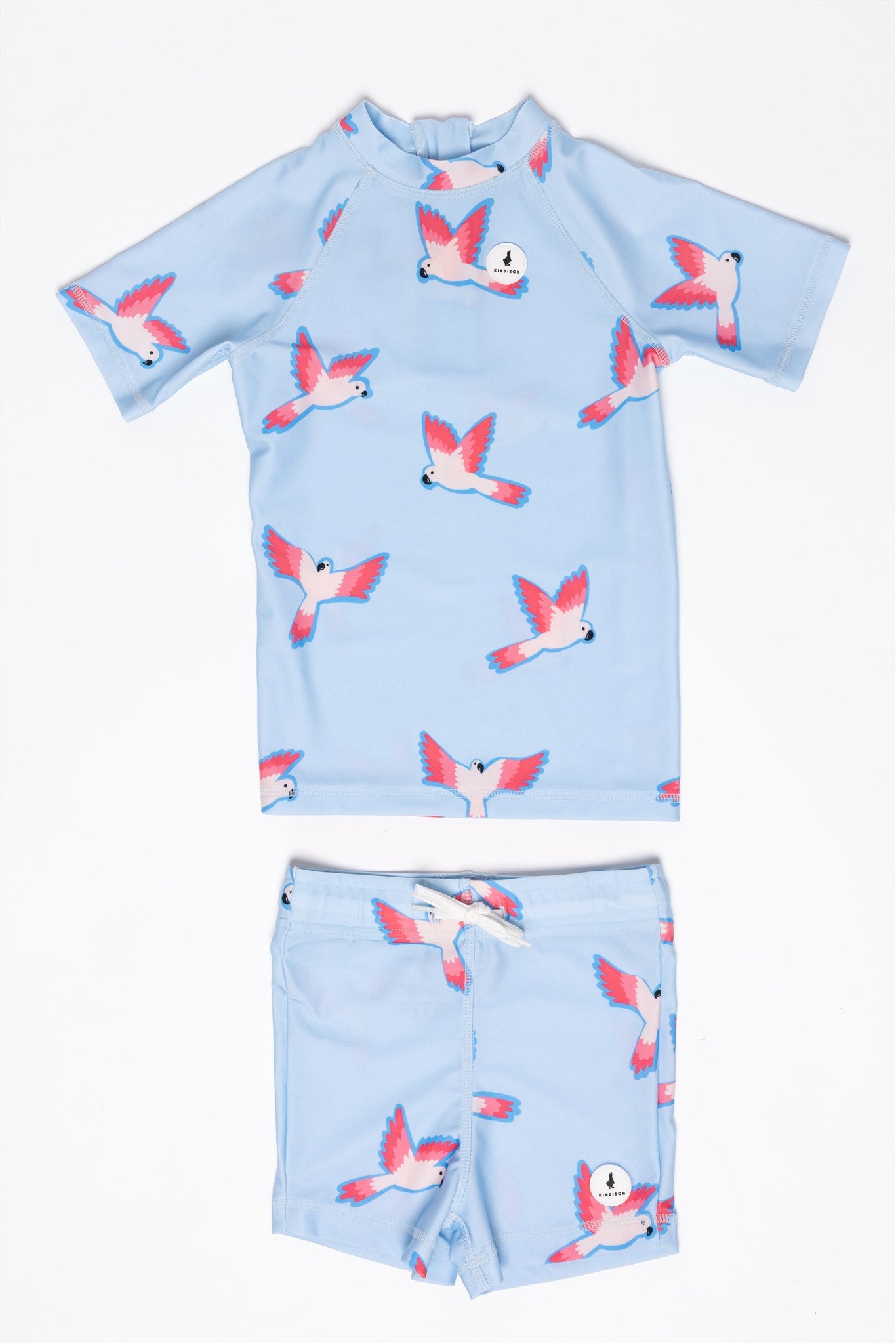 The Boys 2-piece PARROT swim set by kindischworld.com includes a light blue short-sleeve shirt and matching shorts with pink and white parrot patterns, made from recycled polyester, shown laid flat on a white background.