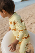 Gelber Baby langarm Badeanzug Pink Leo mit kleinen Leoparden am Strand mit einem Schwimmring – von KINDISCH, UV-Schutz